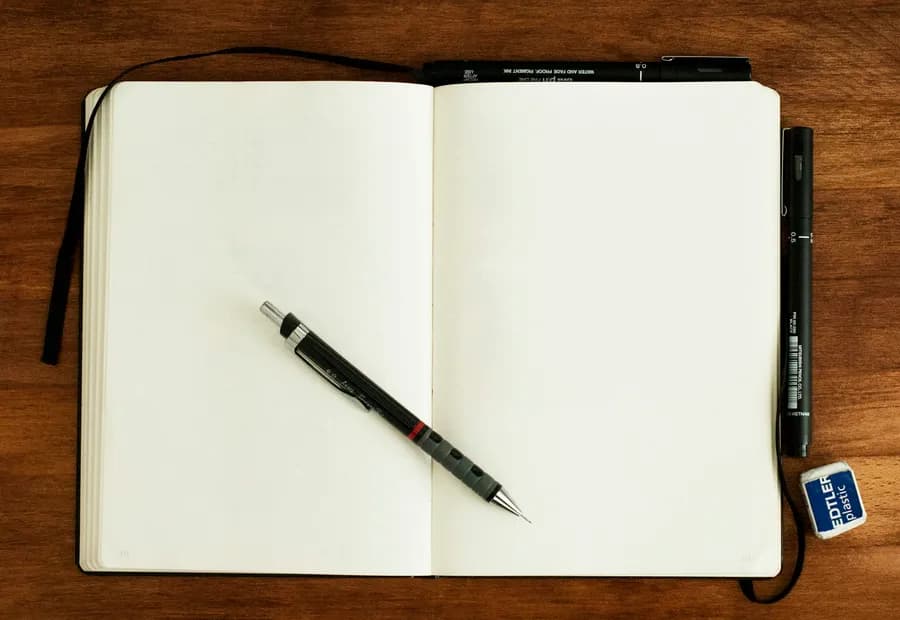 An open notebook and a pen on a wooden desk.